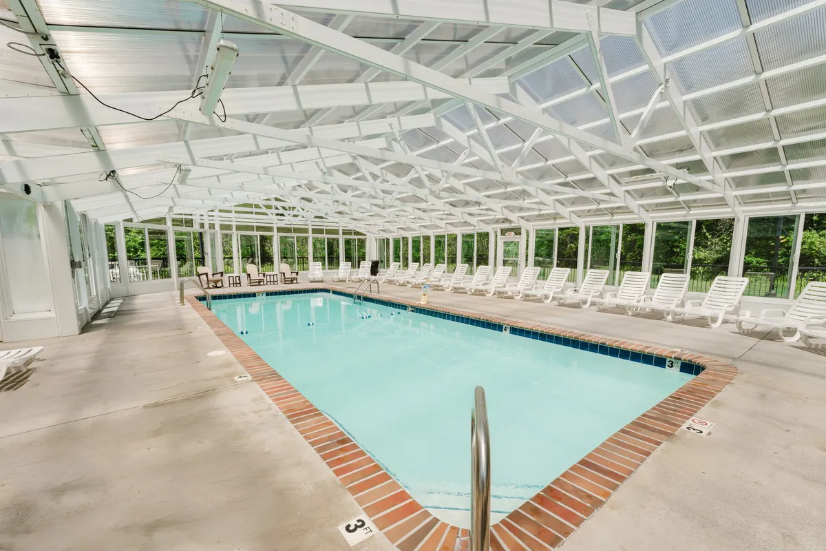 This image showcases the bright indoor swimming pool beneath a striking geometric ceiling, with rows of inviting lounge chairs lining the pool deck. The atmosphere is tranquil, with natural light streaming in, highlighting the spacious and modern feel of the indoor amenity.