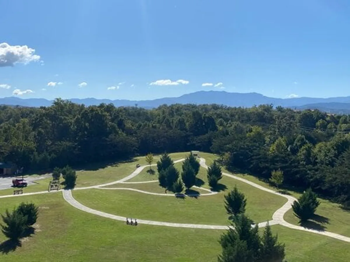 An open grassy area with winding pathways, distant mountains, tall trees, and small groups of people enjoying outdoor activities. The setting is tranquil and encourages exploration, picnics, walks, and community gatherings, highlighting amenities and recreational opportunities close to the property.