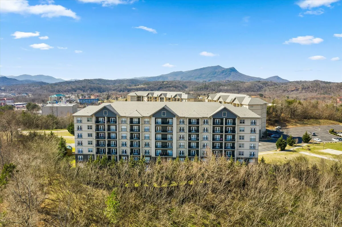 This image shows the exterior of a modern apartment building nestled among greenery, with the distant outline of mountains in the background. The scene conveys a peaceful atmosphere and highlights the natural beauty surrounding the property, suggesting easy access to scenic outdoor experiences.