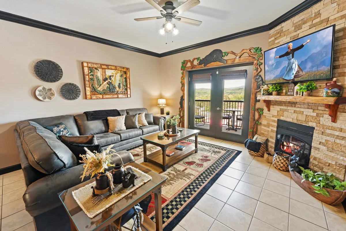 A cozy living room scene with a sofa oriented toward a fireplace and a television. Artwork adorns the wall and a coffee table sits in front of the sofa, fostering an inviting space for relaxation or socializing. The arrangement suggests proximity to a balcony or windowed area, enhancing the sense of light and openness.