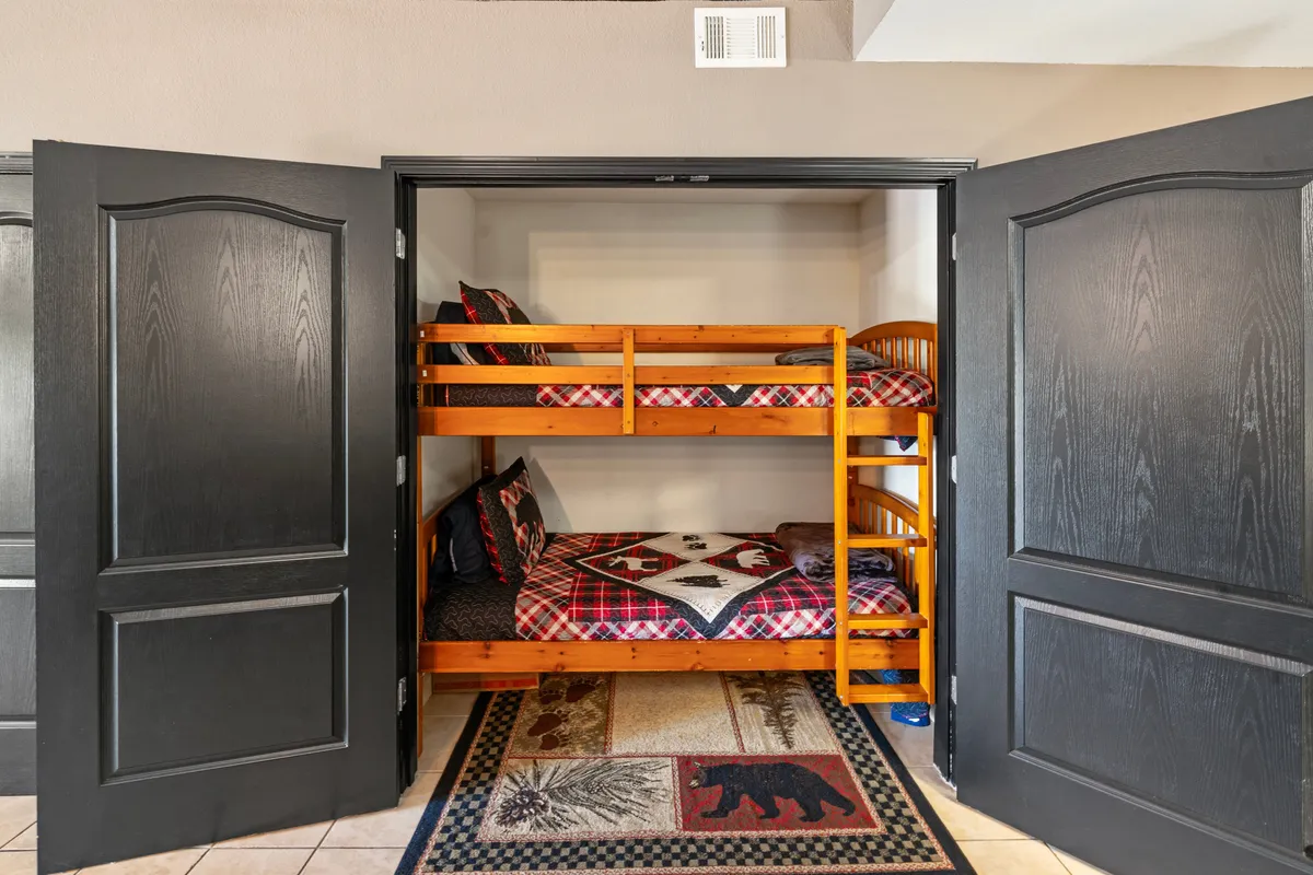 A playful and cozy sleeping nook with twin/twin bunk beds adorned in plaid bedding, and a charming rug with a bear motif. The space is inviting for children, offering comfort and a sense of adventure for little guests.