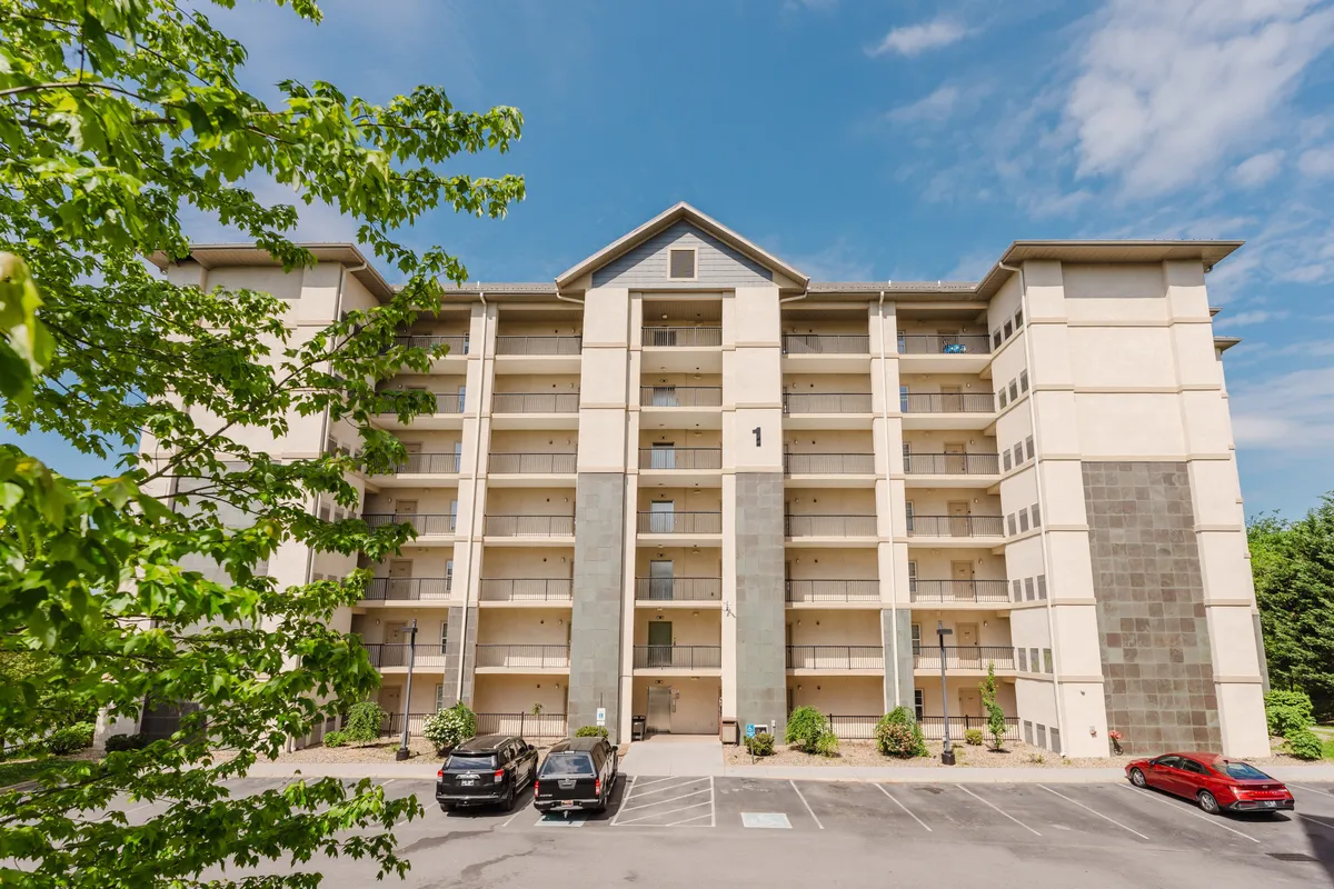 The image features the welcoming facade of the building, clearly showing the entrance and parked cars, with subtle hints of community living. It indicates the convenience of direct-to-property entry and easy parking, alluding to the vacation rental’s hassle-free check-in process.