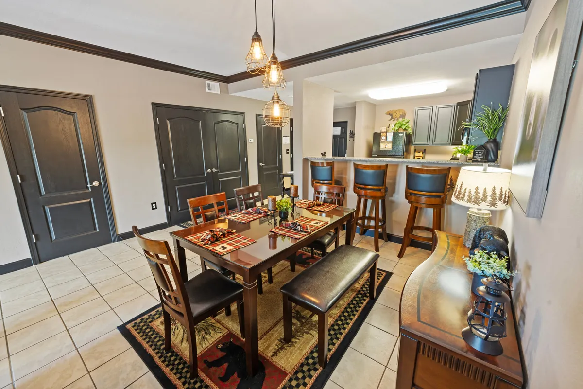 A cozy dining area with a dining table, comfortable bar stools, a decorative lamp, and a kitchen counter in view. The space is inviting and designed for both casual family meals and entertaining guests, with warm lighting enhancing the welcoming atmosphere.