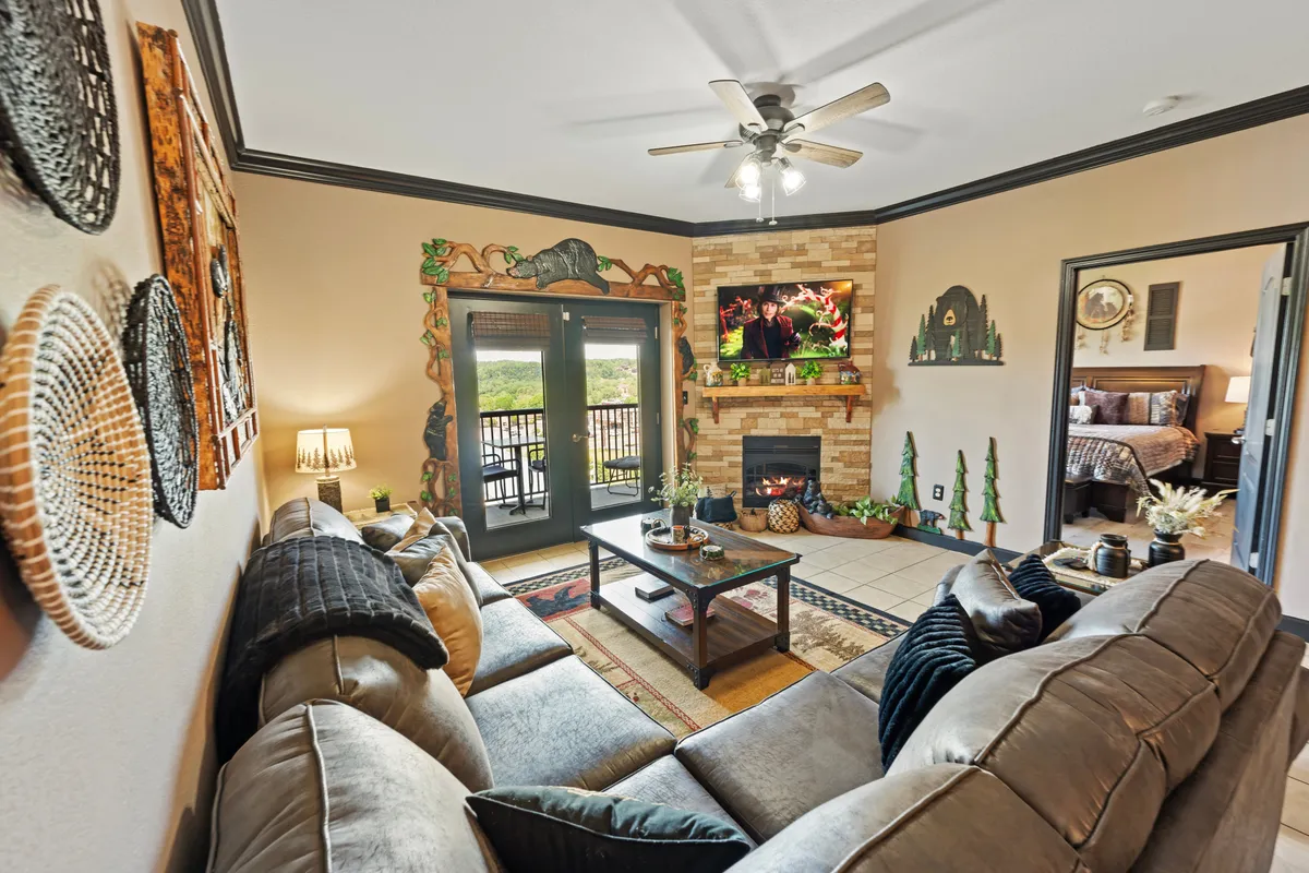 This image features a comfortable sectional sofa, a coffee table, a fireplace, decorative wall art, and a large television. The space feels cozy and inviting, perfect for relaxing or socializing. The fireplace and TV are clearly visible, with hints that the room may connect to a balcony beyond.